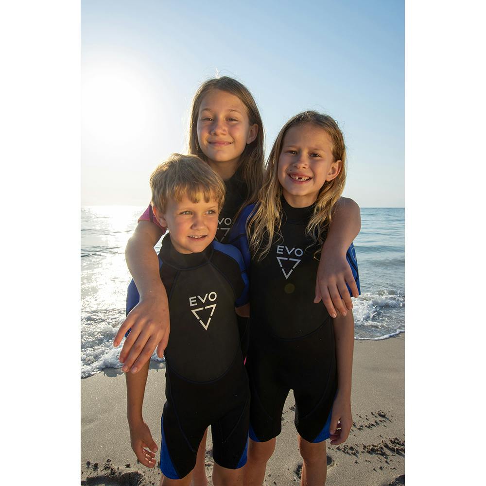 Three kids on the beach wearing the EVO Kid's Shorty wetsuits