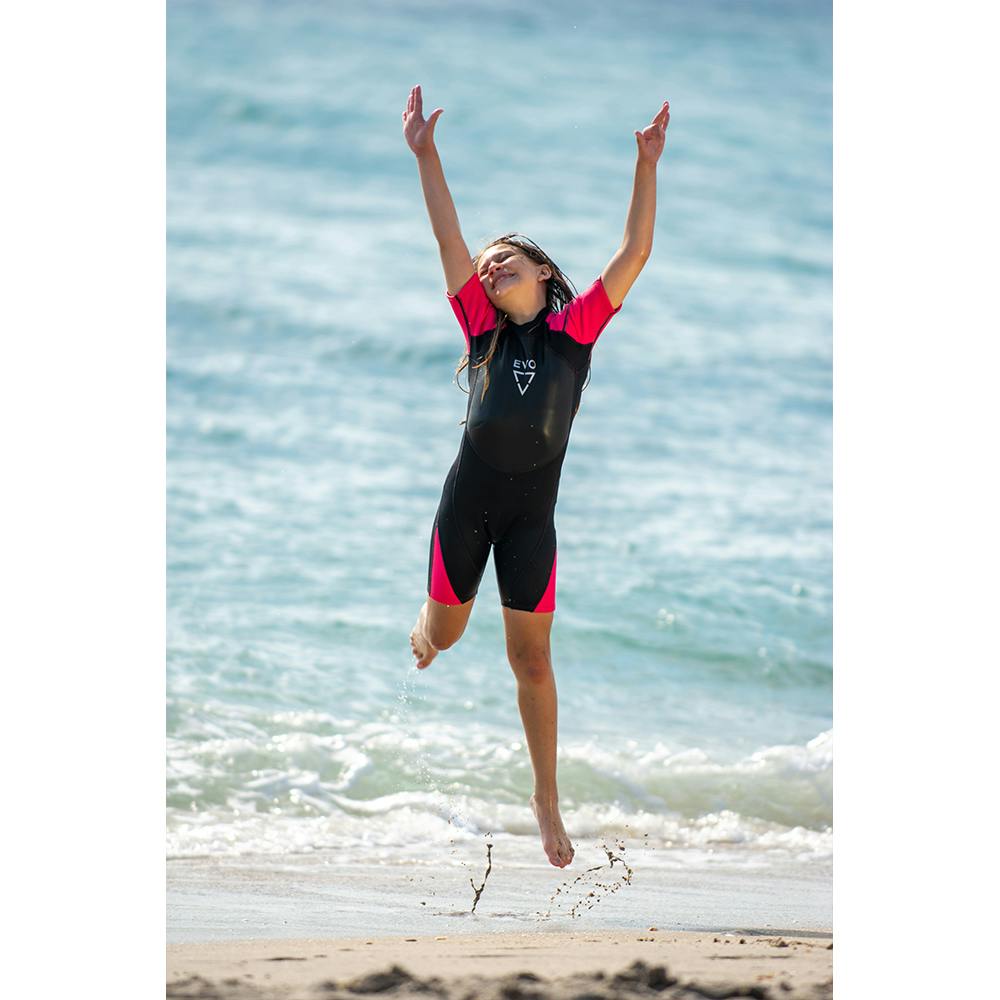 Girl on the beach jumping wearing the EVO Kid's Shorty wetsuits